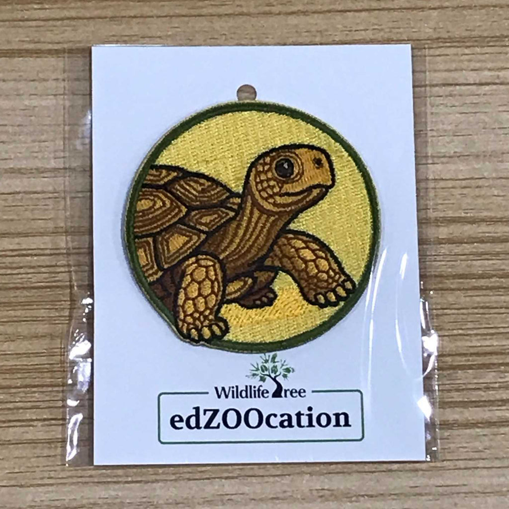 Embroidered turtle patch on a card with 'edZOOcation' branding, placed on a wooden surface.